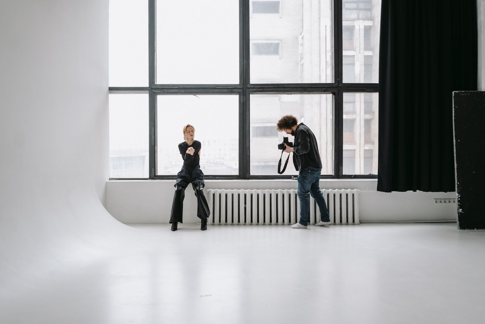 Pusty, jasny pokój z dużym oknem: fotografujący z aparatem i model siedzący na parapecie