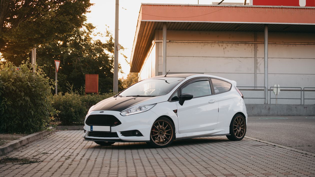 Biały hatchback z czarną maską i dachem zaparkowany na parkingu przy budynku, przód z ukosa