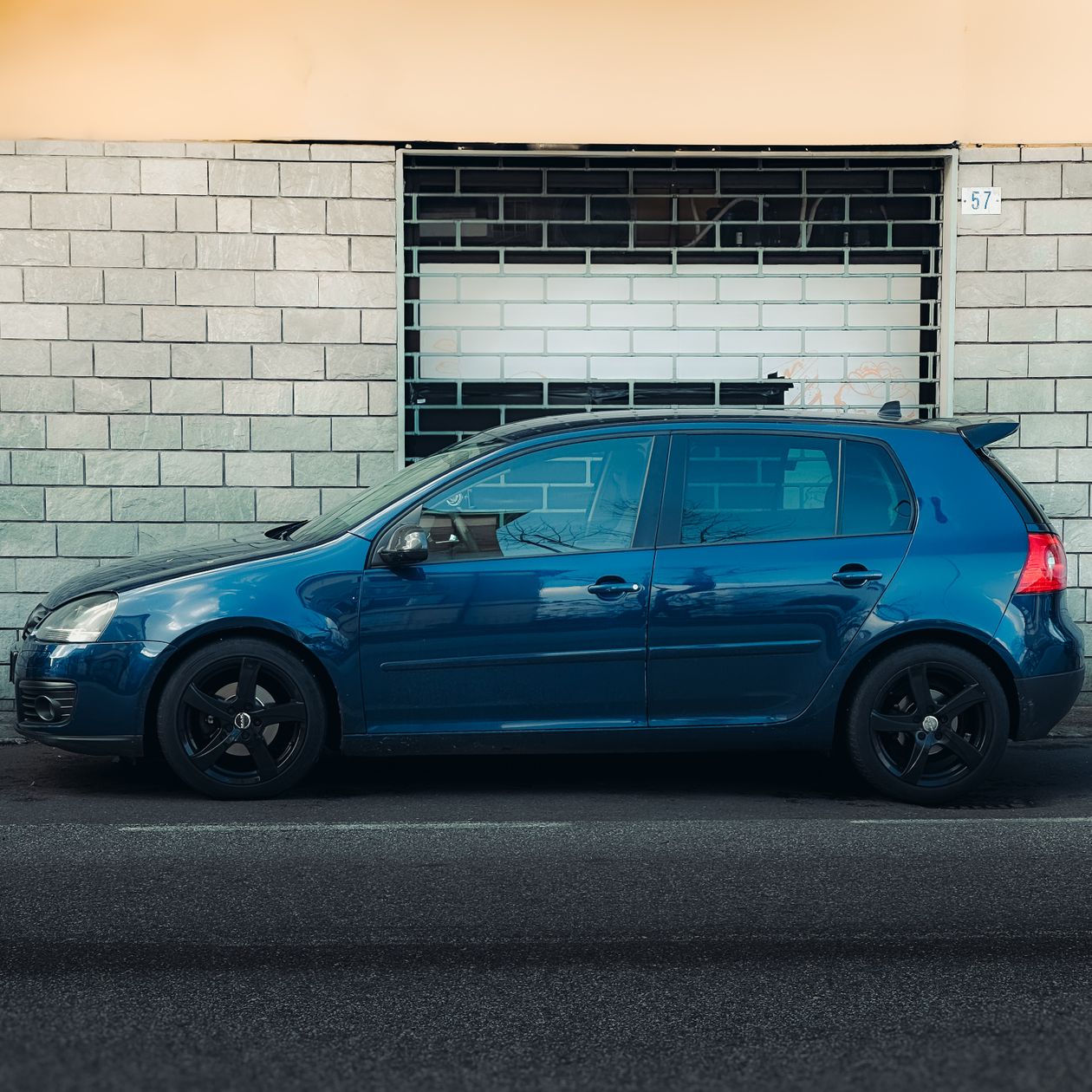 Niebieski hatchback zaparkowany przy ścianie budynku na ulicy miejskiej, widok z boku