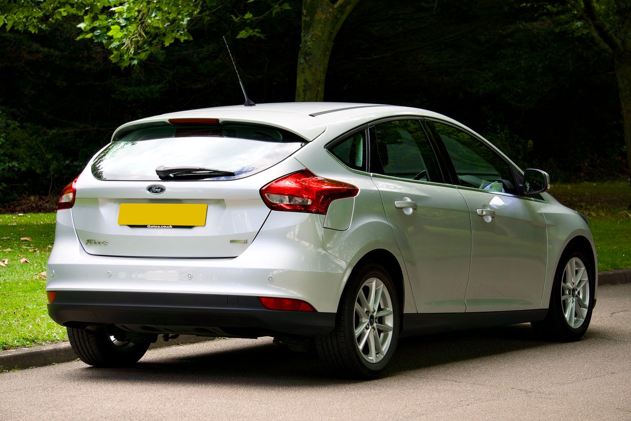 Srebrny hatchback zaparkowany na ulicy przy parku w dzień, tył z ukosa